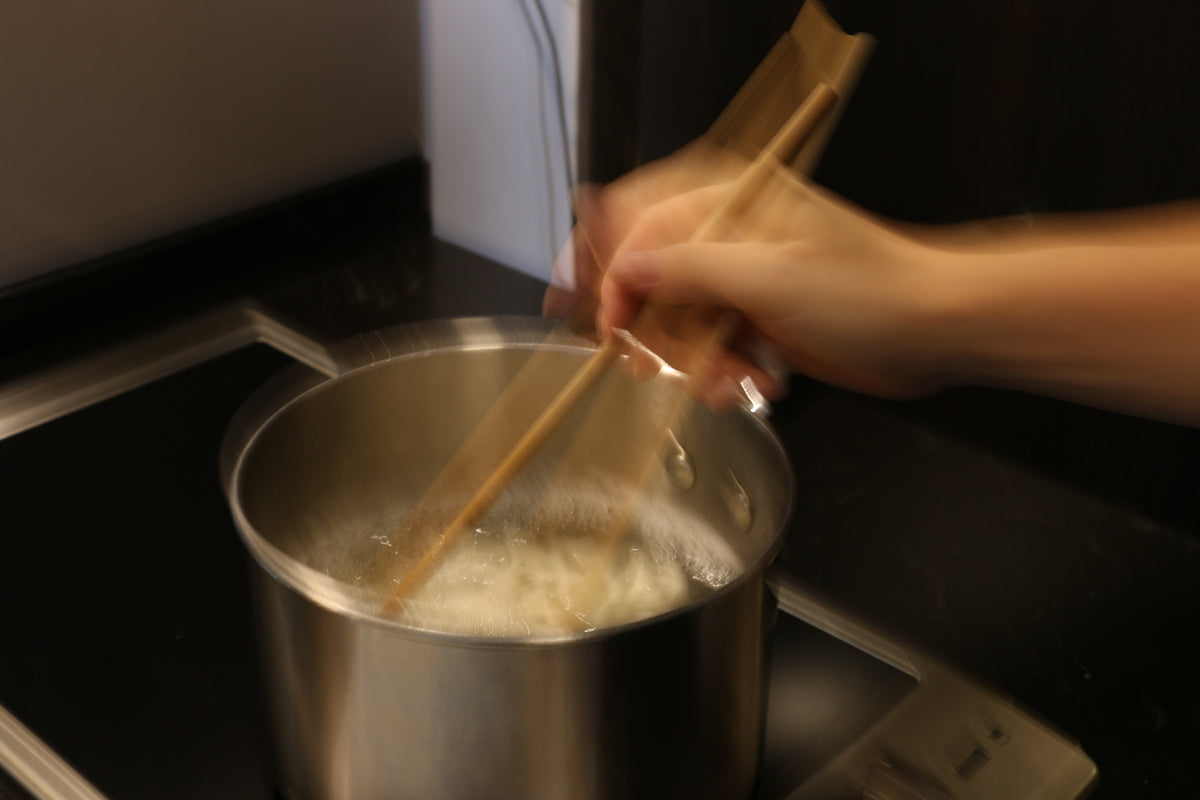 Person stirring noodles in a pot with wooden chopsticks