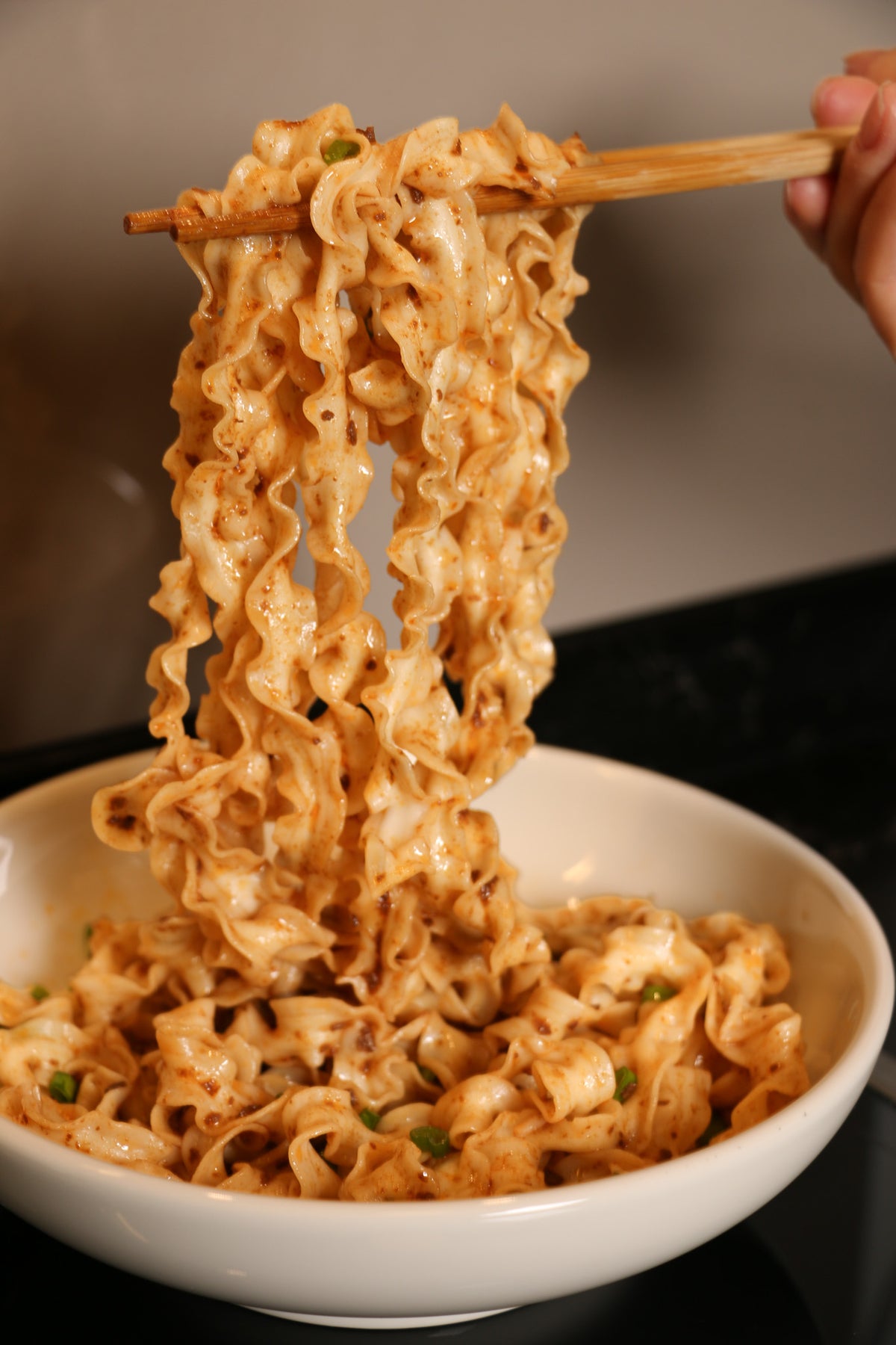 Taiwanese sliced noodles with green onion being lifted with chopsticks